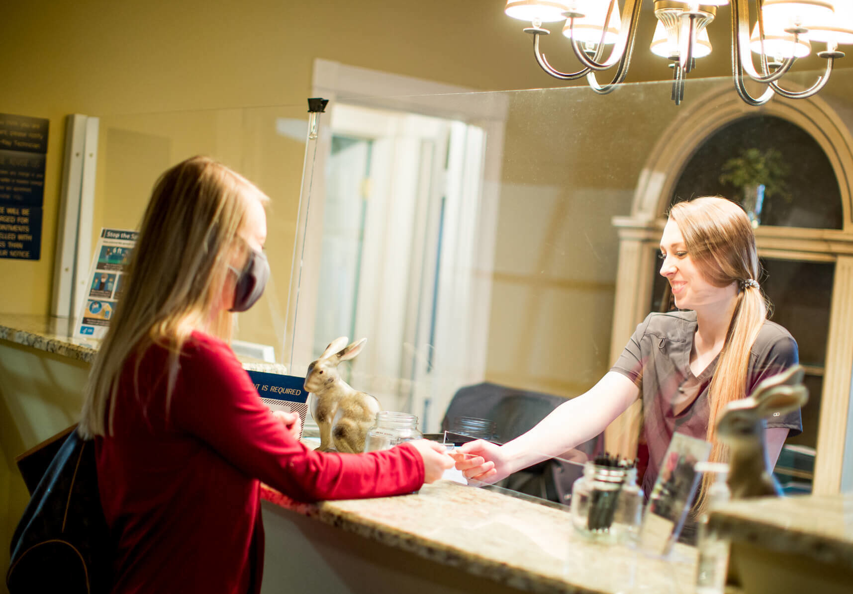 A team member smiles and speaks with a patient at the front desk.